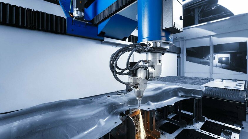 Präzise Laserschneidmaschine bei der Bearbeitung eines Bauteils. Die Maschine schneidet mit hoher Genauigkeit durch ein komplex geformtes Metallteil und erzeugt dabei Funken. Moderne Laserschneidtechnologie für die Fertigung von Automobilkomponenten.