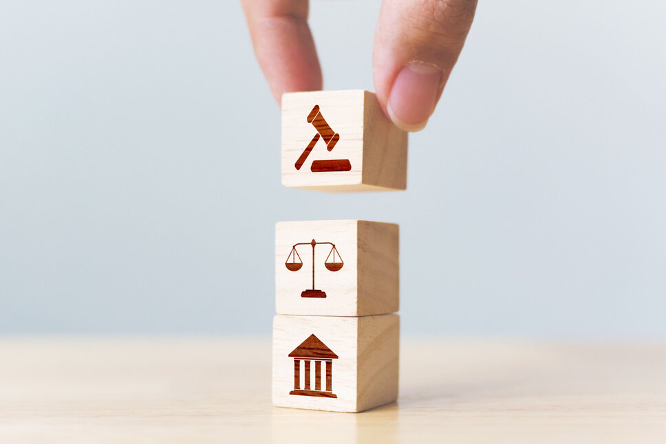 Drei Holzblöcke in Würfelform mit aufgemalten Ikonen, die das Thema Rechtsgerechtigkeit darstellen, symbolisch für Stabilität und Rechtsordnung.
