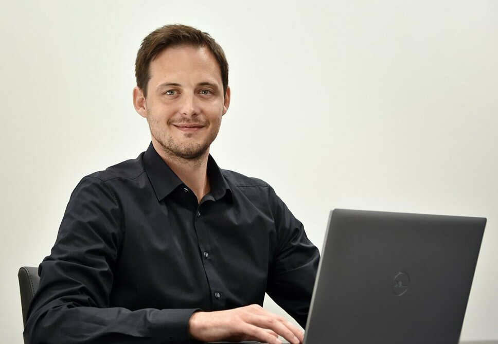 Ondrej Zima, Human Resource Manager der weba Olomouc sitzt avor einem geöffneten Laptop und  lächelt in die Kamera