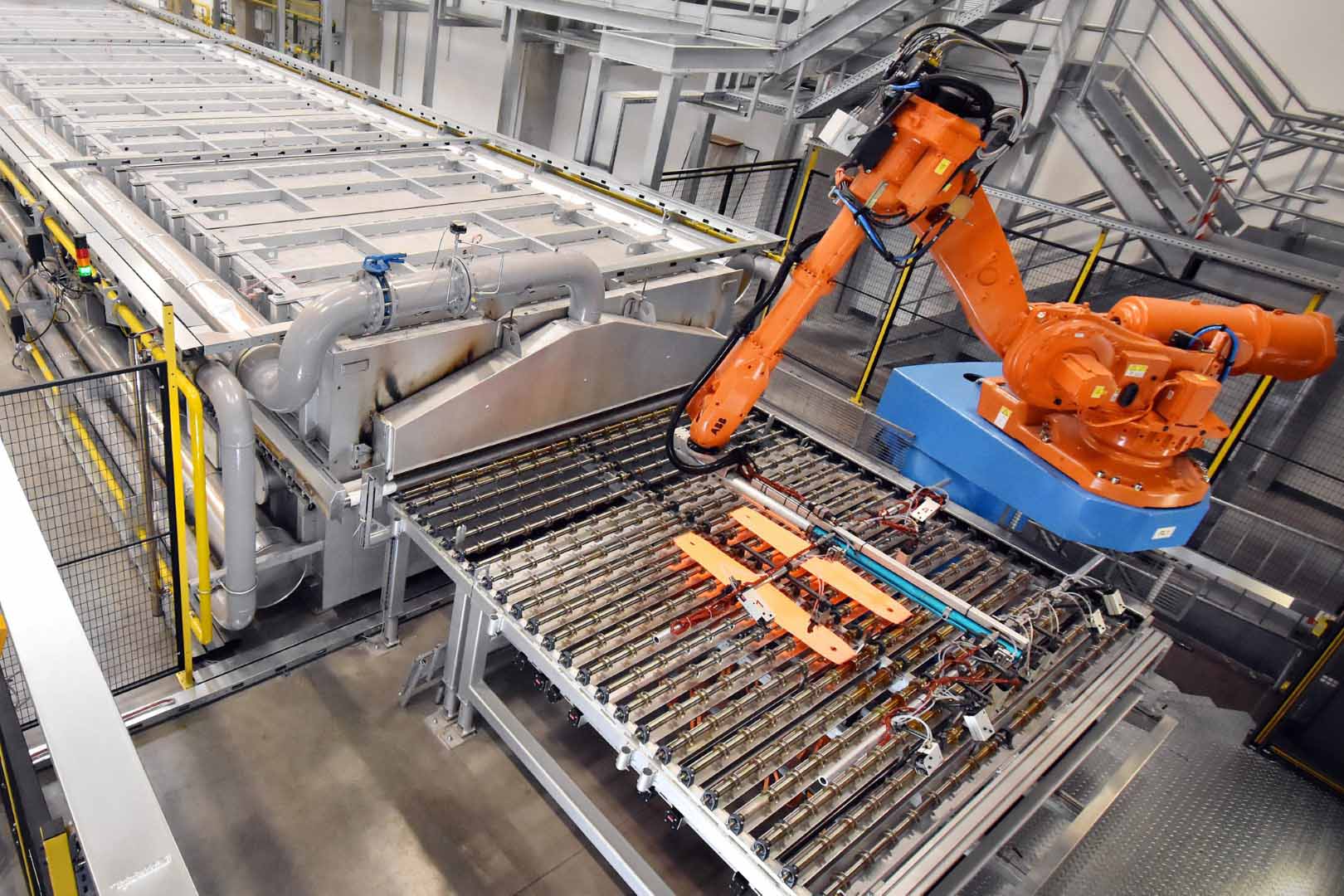 Roboterarm in einer automatisierten Produktionsanlage bei der Warmumformung, der glühend heiße Metallteile von einem Ofen zur Presse transferiert.